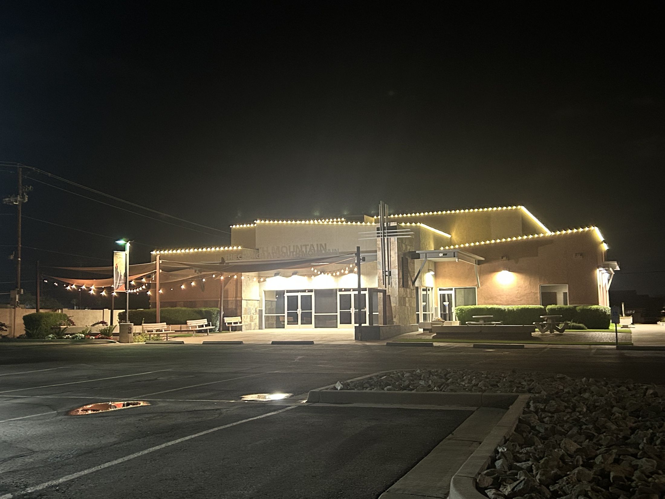 A large Arizona commercial building glowing with warm C9 roofline lighting and bistro string lights at night.