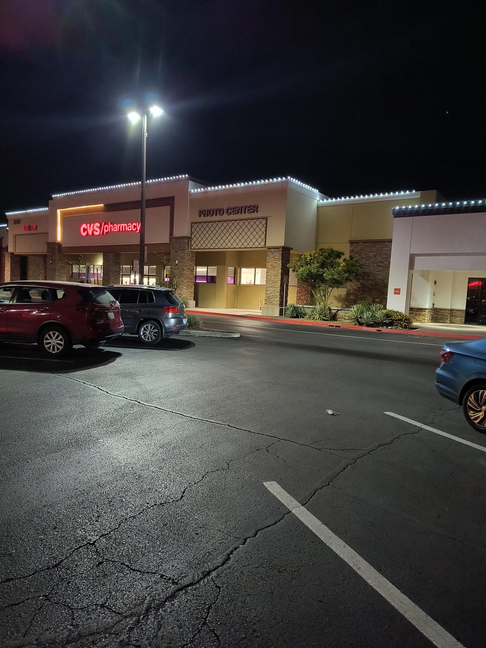 A single crisp line of C9 LED lights along a pharmacy and retail center roofline at night.